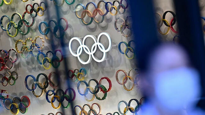 Una persona con mascarilla pasa por delante de varios logos con los aros olímpicos.