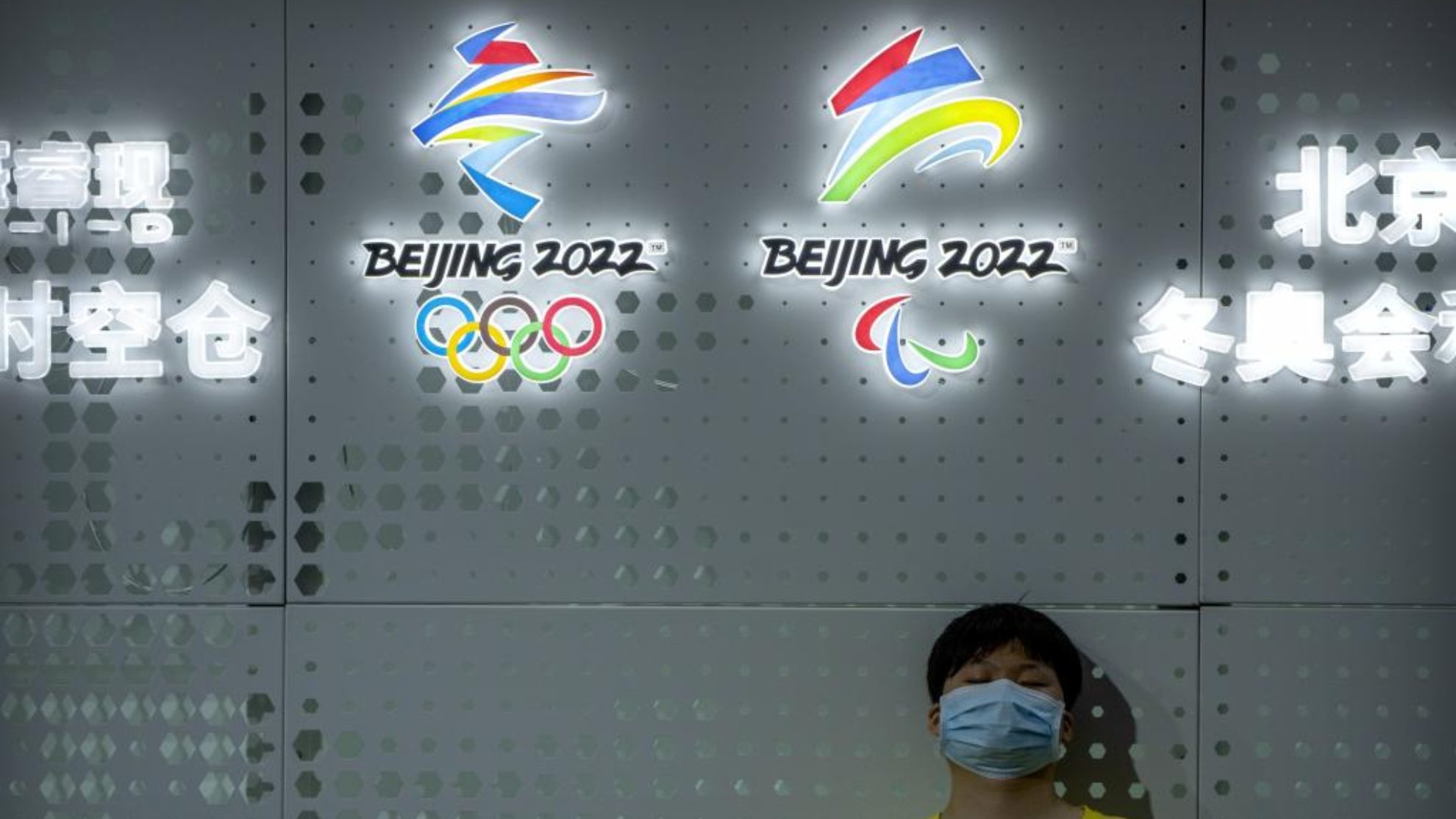 Una persona con mascarilla delante de los logos olímpicos y paralímpicos de Pekín 2022.