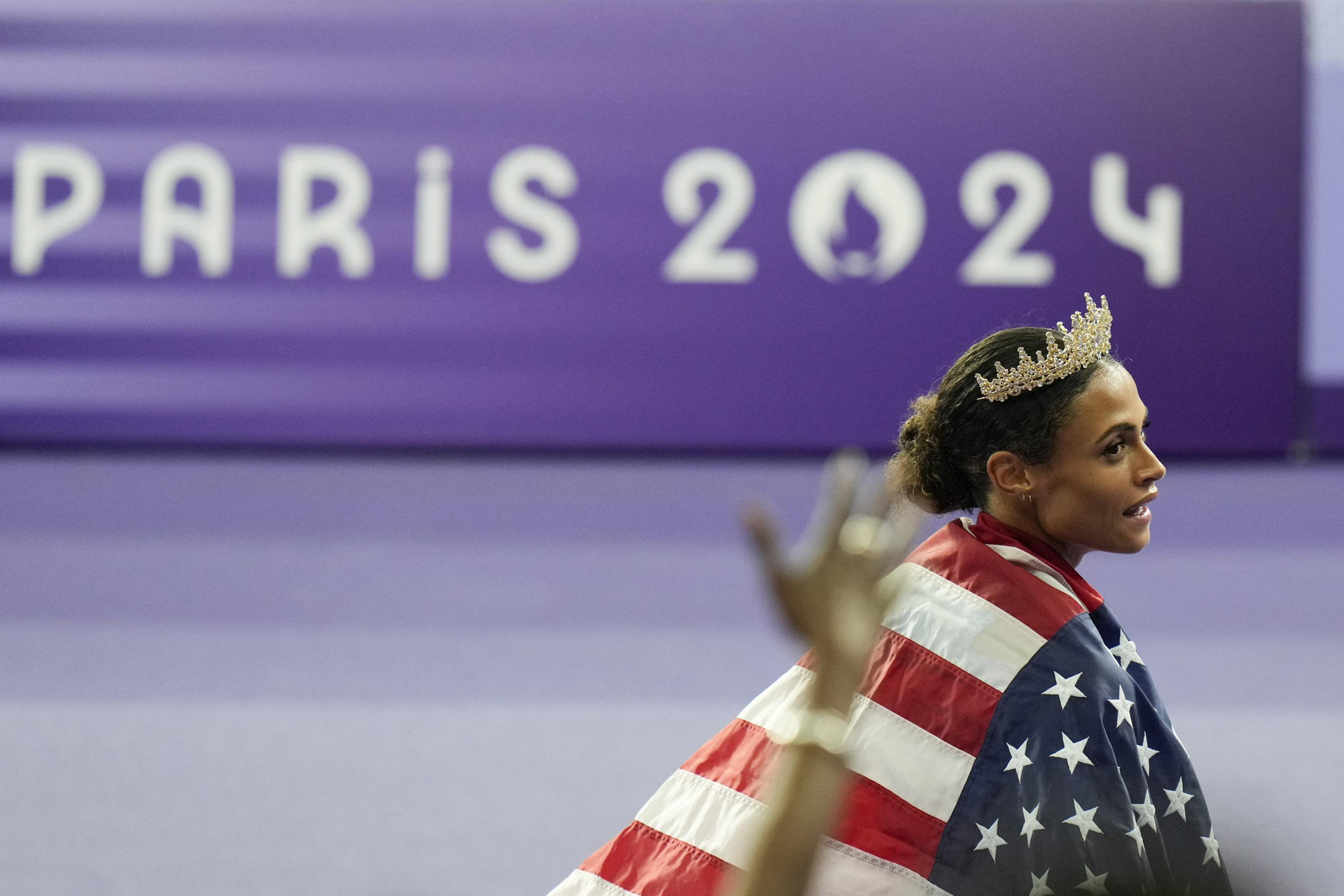 Sydney McLaughlin con una corona y una bandera estadounidense tras imponerse en la final olímpica de los 400 vallas en París 2024.