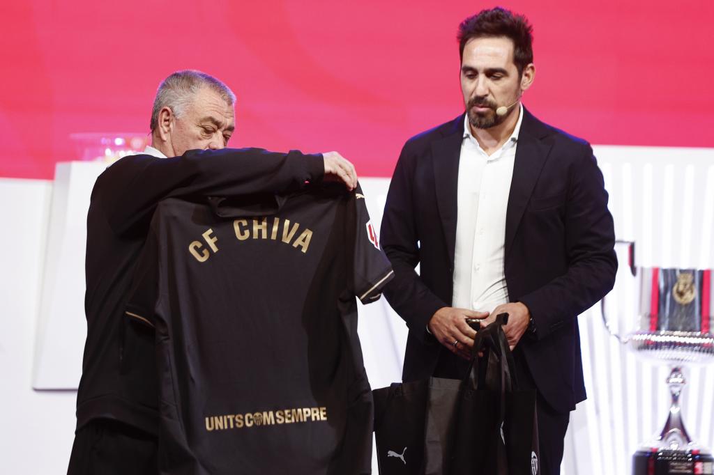 LAS ROZAS (MADRID), 27/11/2024.- Vicente Rodríguez (d), exfutbolista del Valencia y actual embajador institucional, entrega a Domingo Rodríguez, entrenador del Juventud Chiva, una de las camisetas negras del Valencia durante el sorteo para determinar los emparejamientos de la segunda ronda de la Copa del Rey celebrado este miércoles en la Ciudad de Fútbol de Las Rozas (Madrid). Estas camisetas negras se hicieron para el partido de la última jornada de Liga que el Valencia disputó contra el Betis, como símbolo del apoyo a los afectados por la dana que asoló la Comunidad Valenciana el pasado 29 de octubre. Rodríguez declaró este miércoles que desde su entidad van a "ayudar en todo lo posible" a los clubes afectados por la dana. EFE/ Rodrigo Jiménez