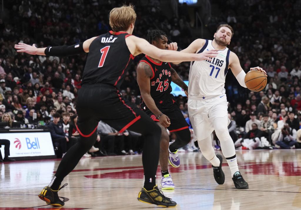 Dallas Mavericks' Luka Doncic (77) is fouled by Toronto Raptors' Davion Mitchell (45) as Raptors' Gradey Dick (1) defends during second-half NBA basketball game action in Toronto, Saturday, Dec. 7, 2024. (Nathan Denette/The Canadian Press via AP)