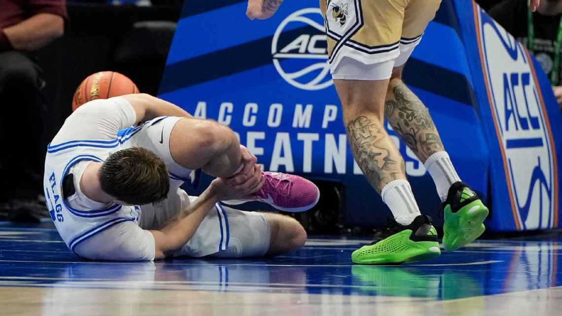 Cooper Flagg se lleva las manos al tobillo izquierdo después de lesionarse.